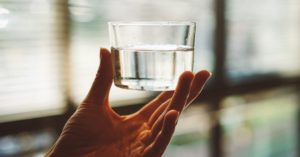 Das Bild zeigt eine Hand die ein Wasserglas hochhält als Sinnbild für hochwertiges zellverfügbares Wasser als Trinkwasser