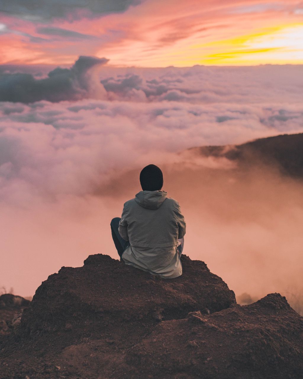 Das Bild zeigt einen Menschen auf einer Bergspitze über den Wolken als Sinnbild für die Pause am Etappenziel auf deinem Abnehm-Weg