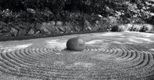 Das Bild zeigt einen runden Stein in einem gepflegten Sandbeet im Garten als Sinnbild für verschiedene Meditationen rund um den 