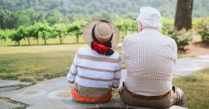 Das Bild zeigt zwei glückliche Senioren, die in einem Garten sitzen und die grüne Natur genießen, als Sinnbild dafür, wie die Ansätze und Methoden der Achtsamkeit beim achtsamen Altern helfen können, alle Veränderungen des Älterwerdens positiv aufzunehmen.