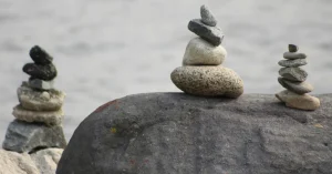 Das Bild zeigt drei kleine Türmchen aus einzelnen Steinen am Meer als Sinnbild für deine Möglichkeiten, mit der Kraft der Meditation deine osteopathische Behandlung für mehr Entspannung und Wohlbefinden zu unterstützen.