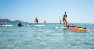 Das Bild zeigt zwei junge Frauen beim Windsurfen lernen in ihrem Urlaub am Mittelmeer.