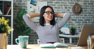 Das Bild zeigt eine erfolgreiche und glückliche Frau im Büro als Sinnbild dafür, wie du als Leistungsträger:in mit der richtigen Körperarbeit und Atemtechnik wieder zu mehr Wohlbefinden und Leistungsfähigkeit finden kannst.